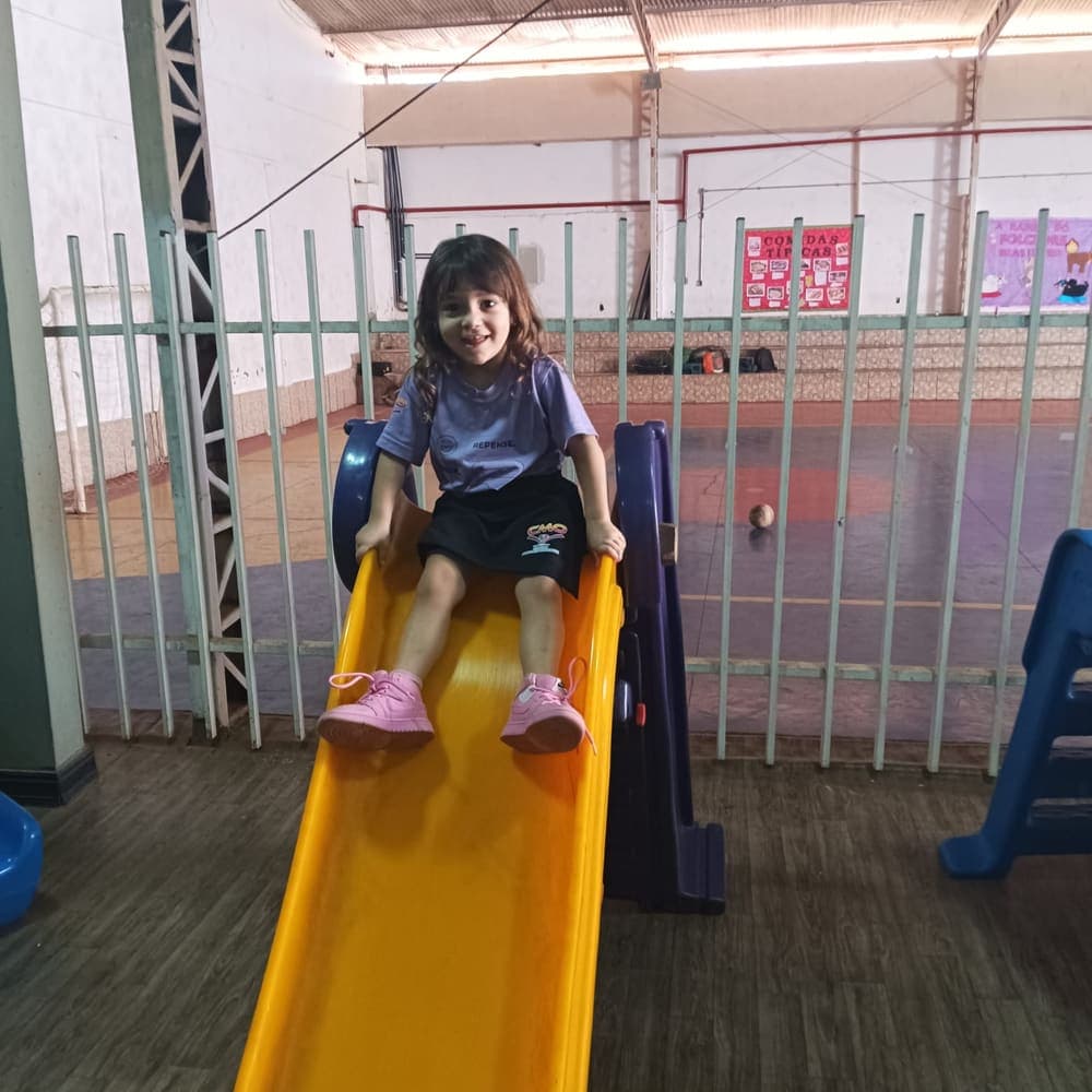 Menina sorrindo no escorregador do pátio da Educação Infantil