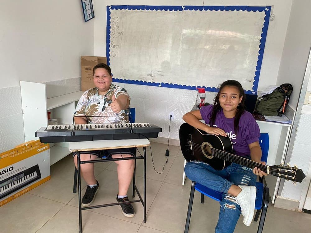 Aluna tocando violão ao lado do professor de música