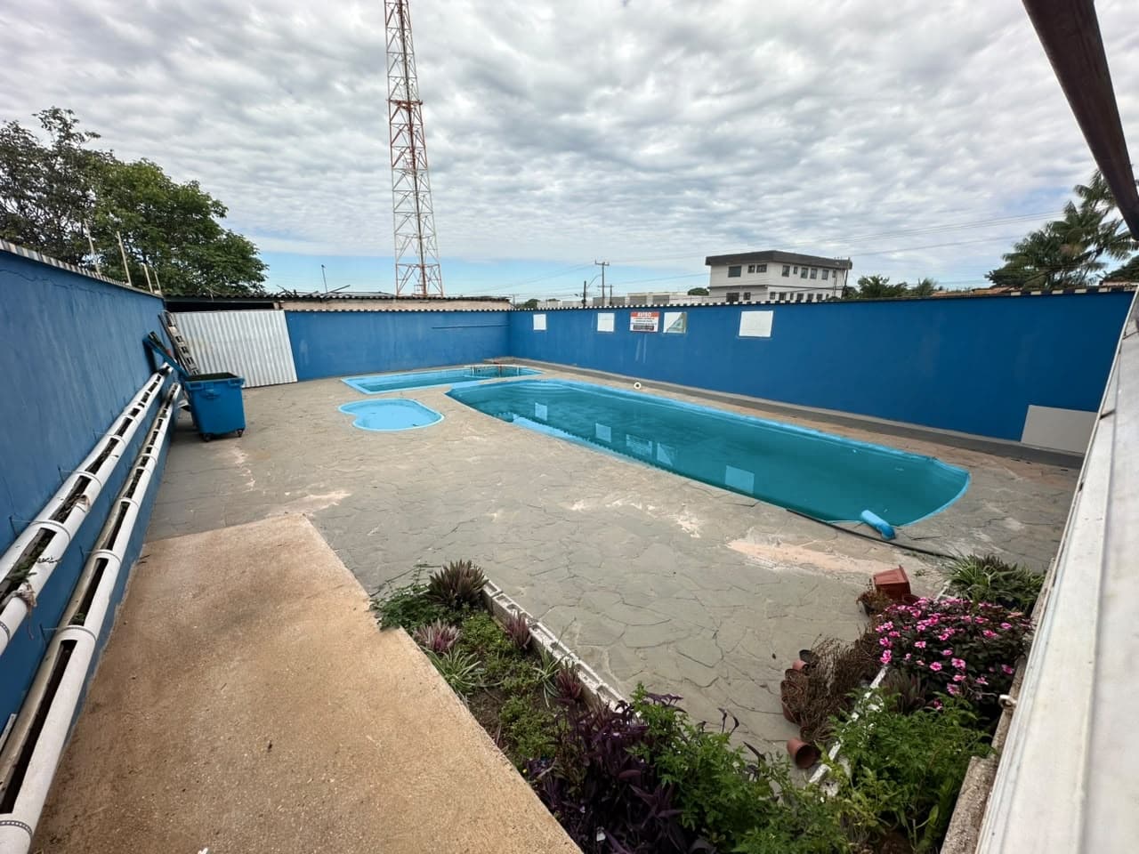 Piscina do colégio cercada por muro azul e canteiro de flores
